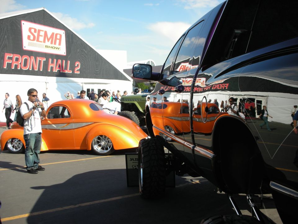 Orange hot rod coupe beside a black lifted truck at the SEMA Show