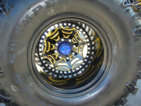 1998 Ford Crown Victoria - Head-on view through a tall Swamper off-road tire at a black-and-yellow web-spoke beadlock wheel with blue center cap.