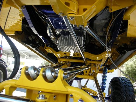 1998 Ford Crown Victoria - Underside of a yellow lifted vehicle showing chrome tubular links, blue accents, and a finned aluminum component.