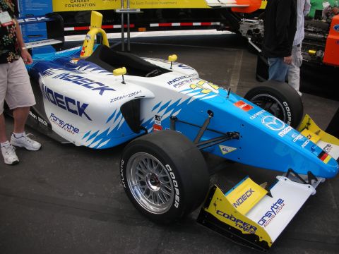 1998 Ford Crown Victoria - blue-and-white open-wheel formula race car with Indeck and Cooper Tires livery displayed indoors at an exhibit.
