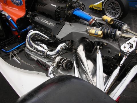 1998 Ford Crown Victoria - exposed rear of an open-wheel race car reveals a Ford Cosworth engine with chrome exhaust headers and coilover suspension.