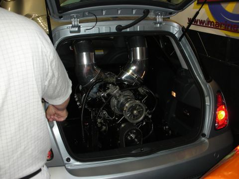 1998 Ford Crown Victoria - twin-turbocharged engine with large chrome intake pipes is built into the rear cargo area of a silver hatchback.