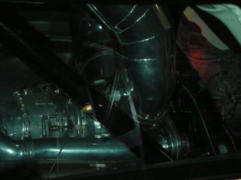 1998 Ford Crown Victoria - dimly lit, reflective view of a polished engine bay with exhaust pipes seen through a glass panel.