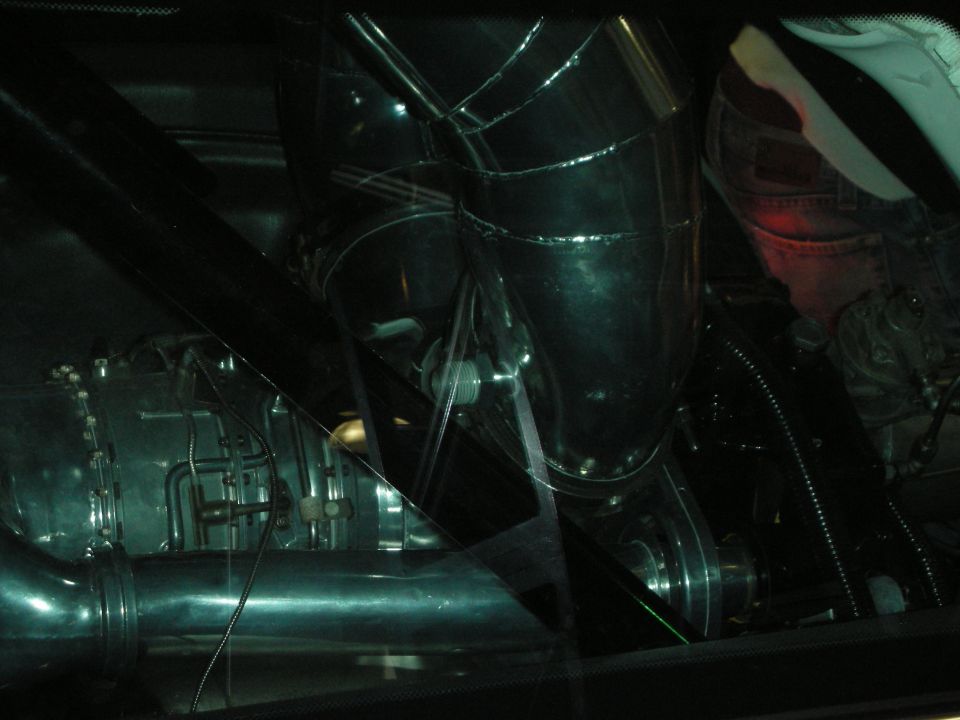 Dark, dim view of a polished engine and exhaust components through glass