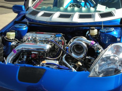 1998 Ford Crown Victoria - blue car's open engine bay shows a polished intake manifold, hard pipes, and a large single turbocharger in sunlight.