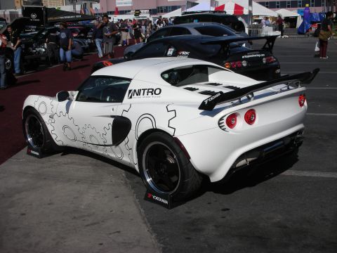 1998 Ford Crown Victoria - white Lotus sports car wrapped with gear graphics and a rear wing sits in an outdoor show lot.