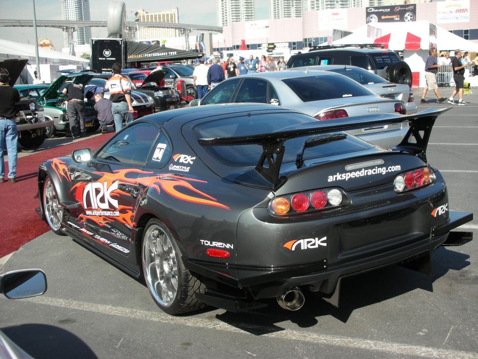 Black Toyota Supra with flame graphics and tall rear wing in show lot