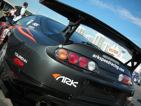 1998 Ford Crown Victoria - close-up of a black Toyota Supra's rear quarter shows its round taillights, decals, and large rear wing.