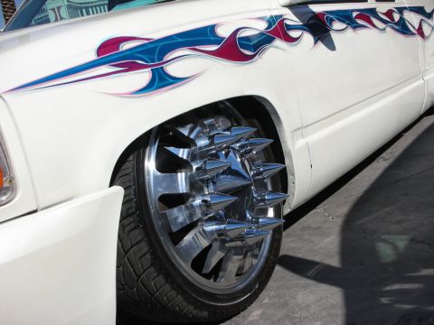 1998 Ford Crown Victoria - chrome dually wheel fitted with pointed spiked lug caps sits under a white pickup with flame graphics.