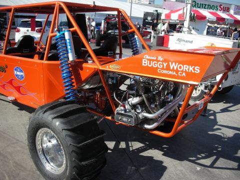 1998 Ford Crown Victoria - orange tube-frame off-road buggy by Buggy Works shows blue coilovers and a mid-mounted engine at an outdoor show.