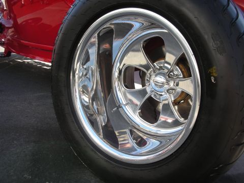 1998 Ford Crown Victoria - close-up of a polished five-spoke chrome wheel and tire mounted on a red hot rod.