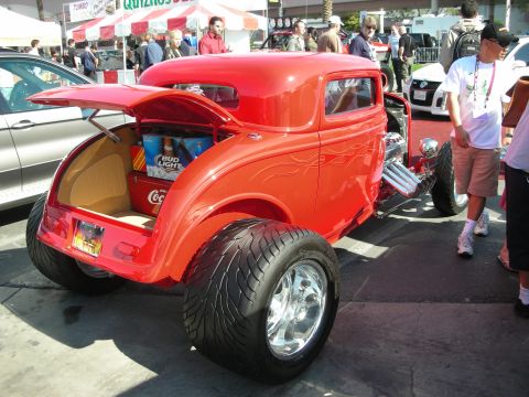 1998 Ford Crown Victoria - rear of a red hot rod coupe sits with its trunk open, revealing a cooler stocked with canned drinks at a show.