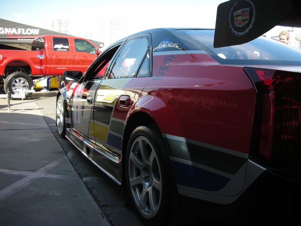 Side rear of a wrapped Cadillac with rear wing parked in a show lot