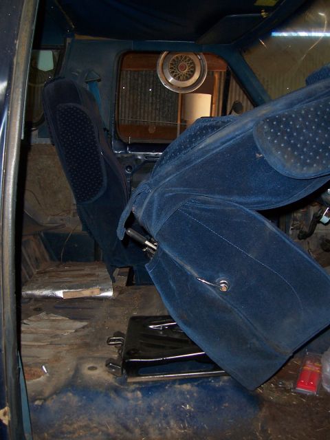 1983 Ford Bronco - Interior of a vehicle with blue velour seats and a hubcap visible through the rear window.