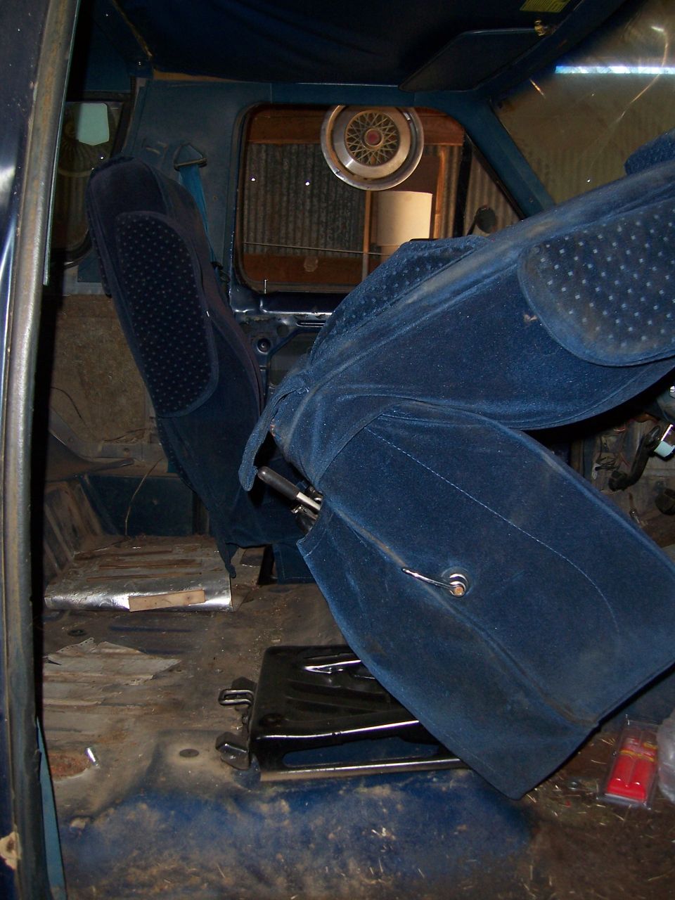 Interior view of a vehicle showing blue velour seats and a hubcap on the rear window