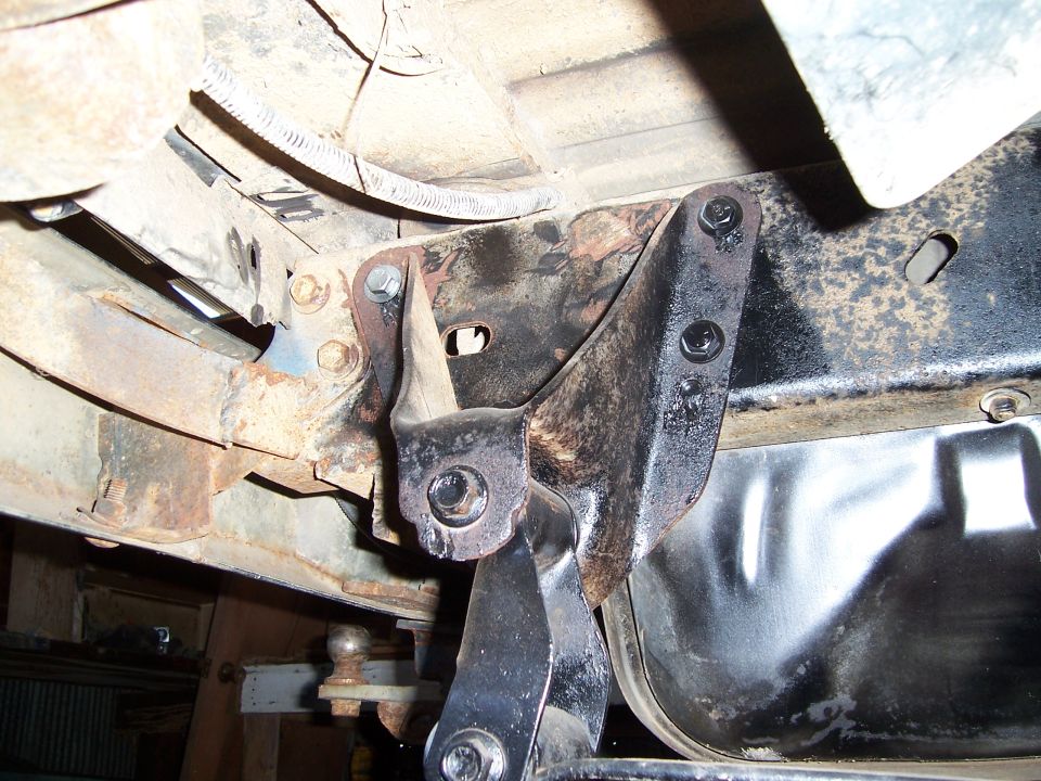 Close-up of rusty vehicle frame with suspension parts attached. Shows a ball hitch underneath