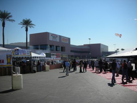 1998 Ford Crown Victoria - Crowds gather on a paved plaza outside the SEMA convention center, lined with palm trees, vendor tents and an overhead blimp.