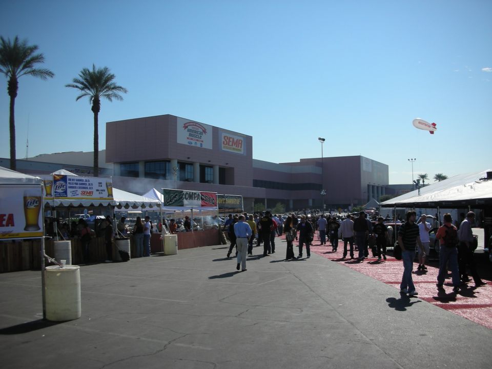 Crowd at outdoor SEMA convention center entrance with palm trees and vendor tents