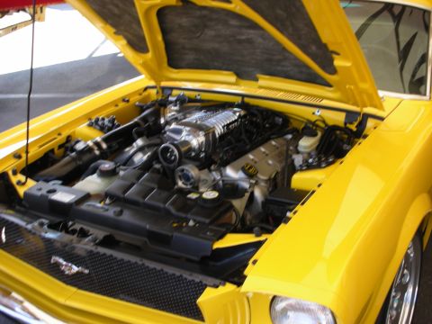 1998 Ford Crown Victoria - open hood of a bright yellow car reveals a supercharged V8 engine bay with chrome and black components.