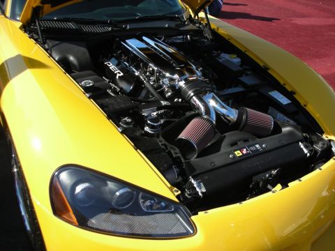 1998 Ford Crown Victoria - yellow sports car's open hood reveals a heavily modified engine with chrome piping and exposed cone air filters.