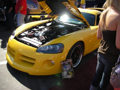 1998 Ford Crown Victoria - yellow Dodge Viper sits with its hood open at an outdoor show as spectators look on.