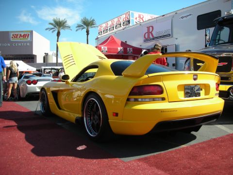 1998 Ford Crown Victoria - Rear three-quarter view of a yellow Dodge Viper with a large rear wing, parked on red carpet at the SEMA show.