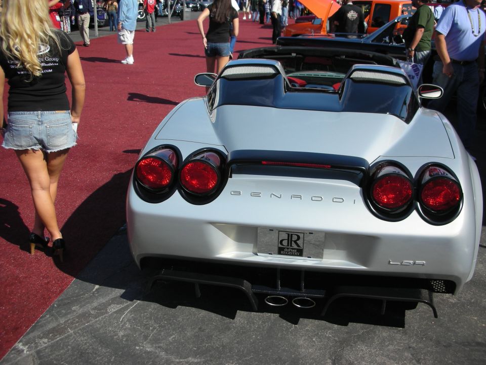 Rear of silver Genaddi convertible with round taillights and woman beside it