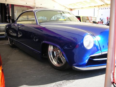 1998 Ford Crown Victoria - deep-blue custom kustom-style coupe sits lowered on chrome wheels beneath a show tent.