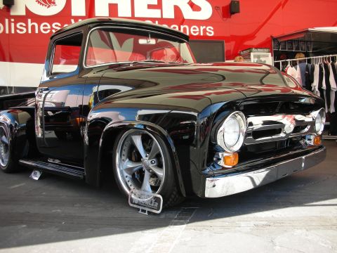 1998 Ford Crown Victoria - glossy black classic Ford pickup truck sits lowered on grey five-spoke wheels in front of a red Mothers banner.
