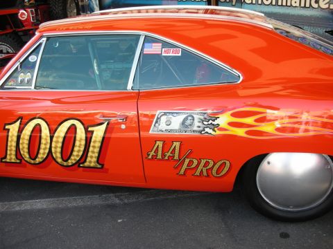 1998 Ford Crown Victoria - Side view of an orange drag car with yellow flames, the number 1001, AA/PRO lettering and a dollar-bill decal.