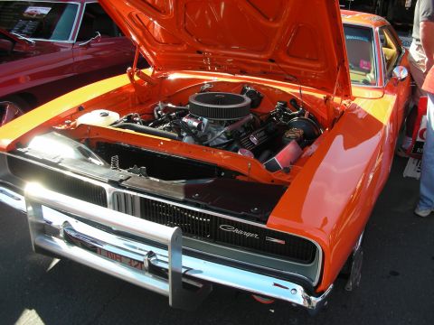 1998 Ford Crown Victoria - orange Dodge Charger sits with its hood open, revealing a chrome-topped V8, at an outdoor car show.