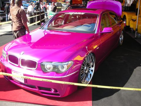 1998 Ford Crown Victoria - bright pink BMW 7 Series sedan sits lowered on chrome wheels on a red carpet behind yellow caution tape.