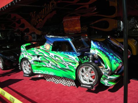 1998 Ford Crown Victoria - custom sports car covered in vivid green and blue flame airbrush artwork sits on red carpet under a show tent.