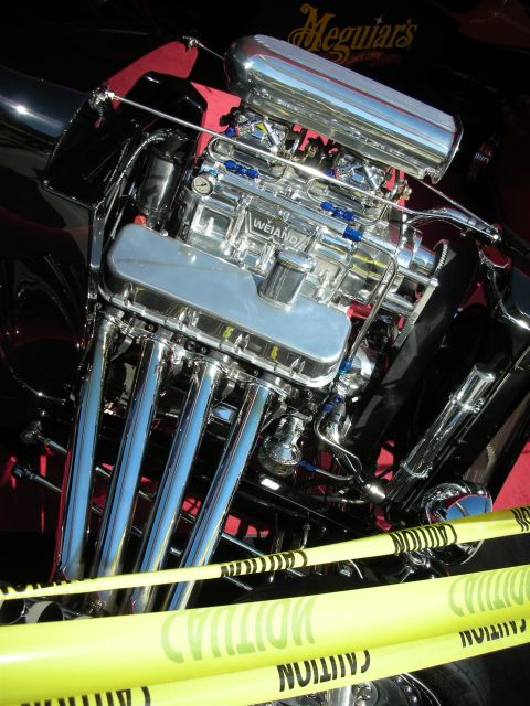 1998 Ford Crown Victoria - heavily chromed supercharged V8 with a Weiand blower and polished zoomie-style headers sits in a hot rod beneath a Meguiar's banner.