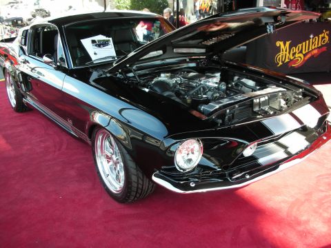 1998 Ford Crown Victoria - black fastback muscle car with twin stripes sits hood-up showing a chromed engine, near a Meguiar's banner.