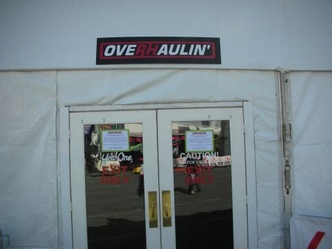 1998 Ford Crown Victoria - Glass double doors marked Caution and Exit Only sit beneath an Overhaulin' sign at a white tent entrance.