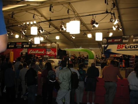 1998 Ford Crown Victoria - crowd gathers under a large tent with bright stage lights, watching past Edelbrock, Mopar and BFGoodrich banners.