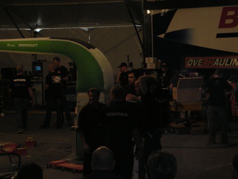 1998 Ford Crown Victoria - Crew members in black shirts gather in a dim shop tent beside a green inflatable downdraft booth and Overhaulin' signage.