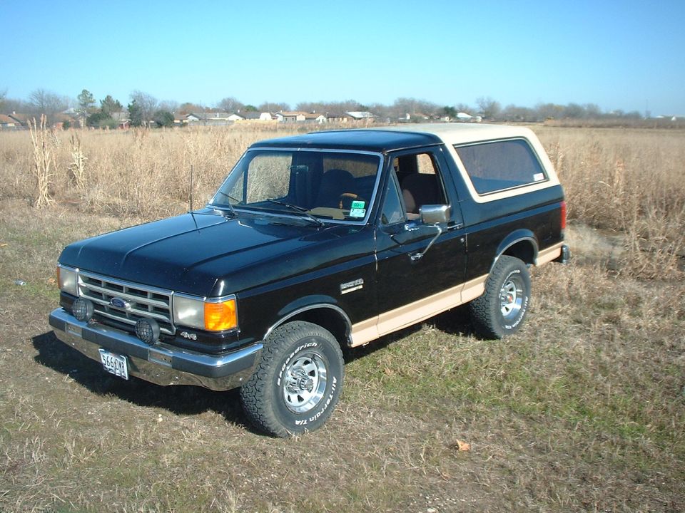 Black and tan Ford Bronco with hardtop and BFGoodrich tires in a field