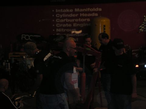 1998 Ford Crown Victoria - Several men gather in a dim shop before a red banner listing intake manifolds, cylinder heads, carburetors and nitrous.