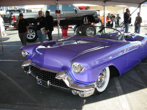 1998 Ford Crown Victoria - purple custom 1950s-style convertible with quad headlights and chrome grille sits under a tent at an outdoor show.
