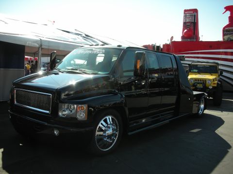 1998 Ford Crown Victoria - black custom medium-duty crew-cab hauler truck on chrome wheels sits beside a yellow Jeep at an outdoor display.