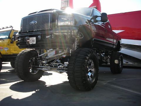 1998 Ford Crown Victoria - lifted Ford Super Duty truck on huge mud tires shows polished chrome suspension links and a STKK license plate.