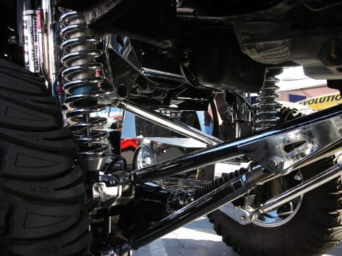 1998 Ford Crown Victoria - Polished chrome coil-over shocks and suspension links fill the undercarriage view of a heavily lifted truck.