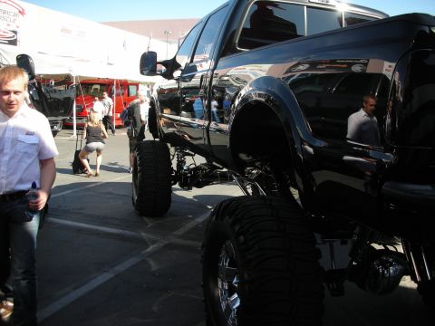 1998 Ford Crown Victoria - heavily lifted black Ford dually truck towers on tall tires in a show lot as people walk past nearby.