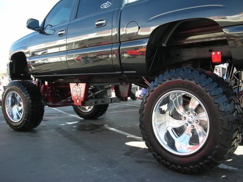 1998 Ford Crown Victoria - lifted black GMC pickup sits high on polished chrome wheels and large off-road tires, showing its red lift linkage.