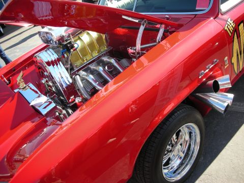 1998 Ford Crown Victoria - red muscle car sits hood-up revealing a chromed engine and polished side exhaust over a chrome wheel.