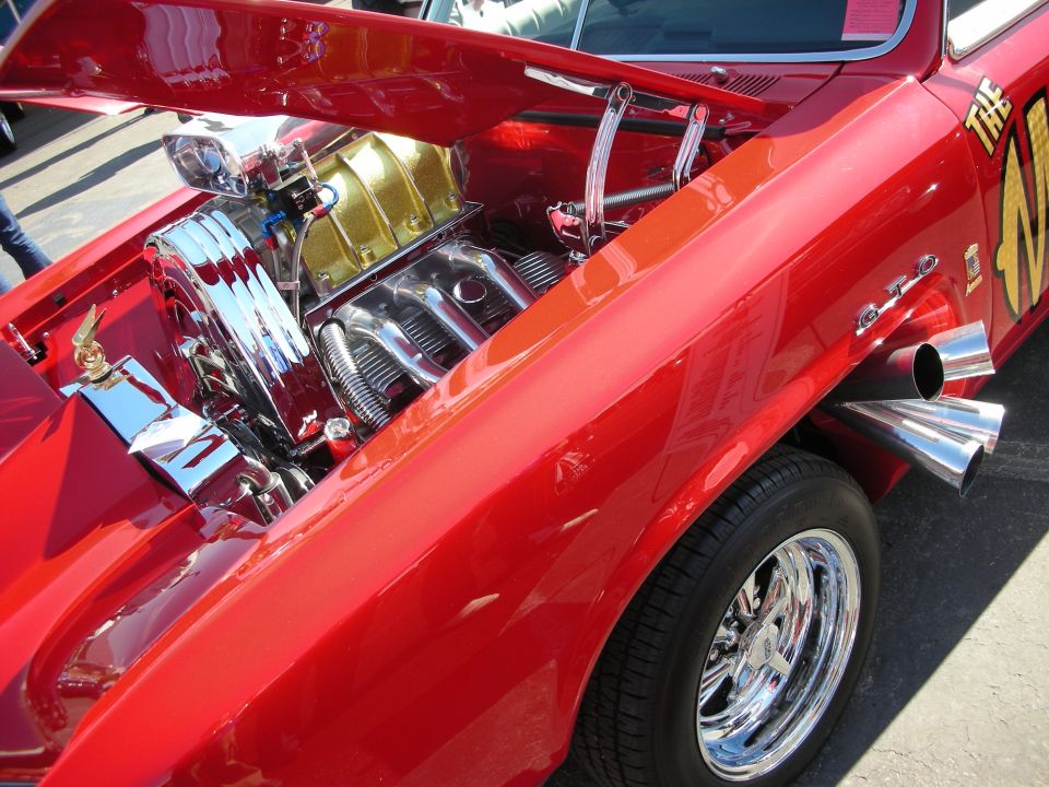 Red muscle car with open hood showing chromed engine and side exhaust