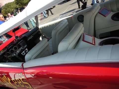 1998 Ford Crown Victoria - red convertible shows off its custom light-gray leather bucket seats and black dash as spectators pass behind.