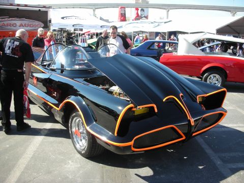 1998 Ford Crown Victoria - black 1960s TV-style Batmobile replica with orange edge trim and bubble canopies draws onlookers at an outdoor show.